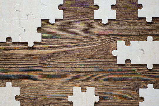 Incomplete wooden puzzles on brown wooden desk, top view, flat lay. Frame with puzzle. The concept of logical thinking, business, conundrum. Business concept with  jigsaw puzzle on wooden background. 