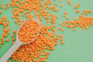 Red lentil in wooden spoon on green background