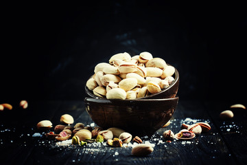 Salted pistachios in a bowl, black background, selective focus