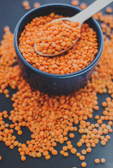 Red lentil in bowl with spoon on black background