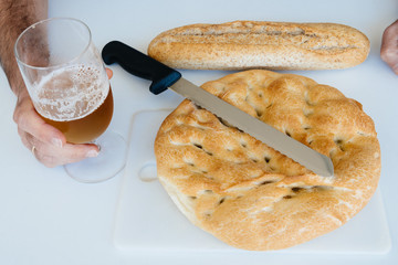 Man with a glass of beer, loaf of bread,  and knife on white table, food closeup