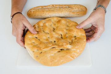 Woman hands holding a loaf of bread on white table, food closeup