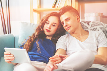 Young couple on sofa at home using pc tablet