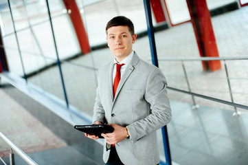 Handsome young businessman in suit using tablet and looking with confidence at the camera.