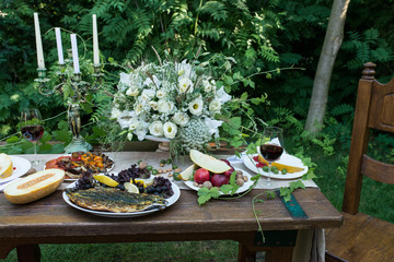 Served table for dinner with red nectarines, red berries, melon, nuts, grilled fish and a glass of red wine