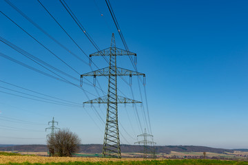 Hochspannungsmast vor blauem Himmel mit Feld im Vordergrund