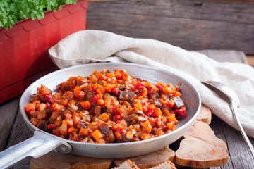 Stewed vegetables (eggplant, peppers, tomatoes) in a frying pan on a wooden table, selective focus, horizontal