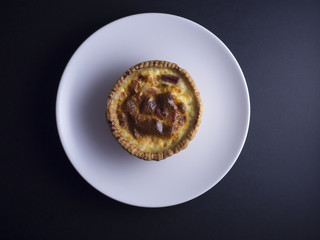 Small quiche lorraine pie on white plate isolated on black background