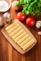 Uncooked cannelloni pasta on cutting board and ingredients