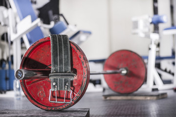 Old school gym interior with equipment, bodybuilding background. Focus on free weight Olympic bar. Weightlifting belt by the side.
