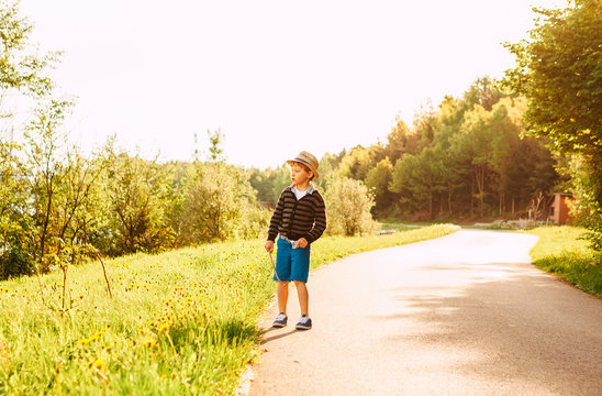 Little boy in straw hat walks on countryside road at the summer evening