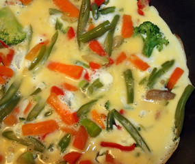 Healthy egg omelet with added vegetables cooking in skillet

