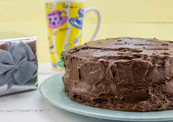 Chocolate cake with frosting on white table with gift and coffee mug