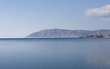 Baikal lake spring landscape view. Snow-covered shore of the lake. Rocky forested coastline.