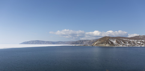 Baikal lake spring landscape view. Snow-covered shore of the lake. Rocky forested coastline. Boundary of ice and open water.