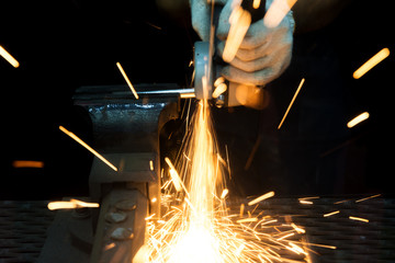 Worker cutting with grinder and welding metal with many sharp sparks in factory