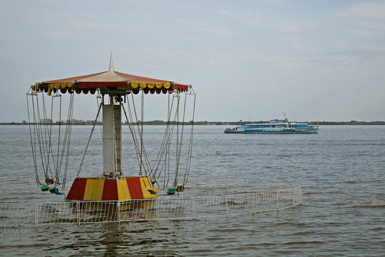 Carousel on the waterfront filled with water during the flood. Pleasure boat sails along the Volga.