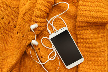 White mobile phone with headphones, soft knitted yellow plaid