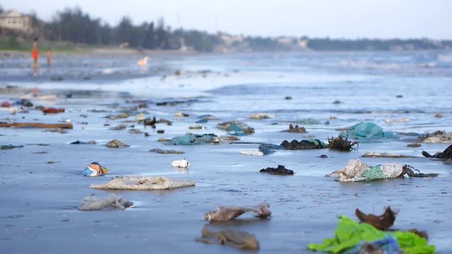 Child playing among the trash and rubbish on sand of seashore.Pan shot. Environmental problem on beach