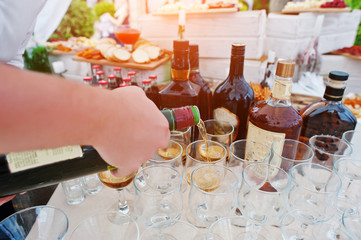 Hand of waiter who pours drinks at glasses on wedding reception.