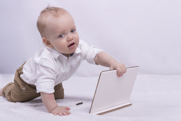 Cute thoughtful boy in white shirt playing with a tablet. Funny infant boy with laptop looks like little businessman