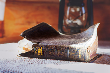 holy bible worn and old on a table with a lantern in the background