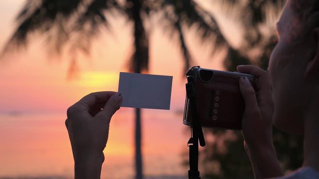 Woman Taking Pictures with Retro Polaroid Camera at Sunset