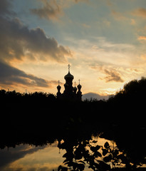 Silhouette of a church against the backdrop of the setting sun and reflection in the lake