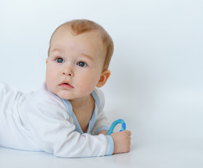 baby child lying on belly weared with teether in mouth.