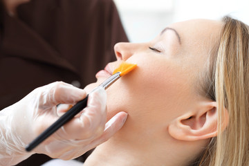 Pielęgnacja skóry, kosmetyczka nakłada pędzelkiem maseczkę na twarz kobiety
