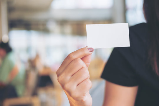 An image of a woman holding and showing empty business card in modern loft cafe