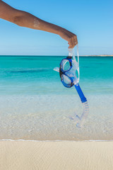 Snorkel set in one hand in front of the blue ocean