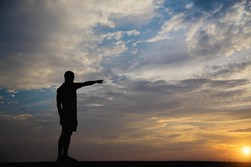 Silhouette of a man with hands point to sky in the sunset.
