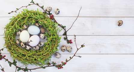 Easter composition of colored chicken and quail eggs in a nest on a white wooden background. Holiday concept with copy space view from above.