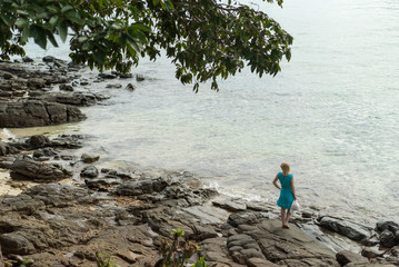 Young woman in blue dress staying on the rocky beach