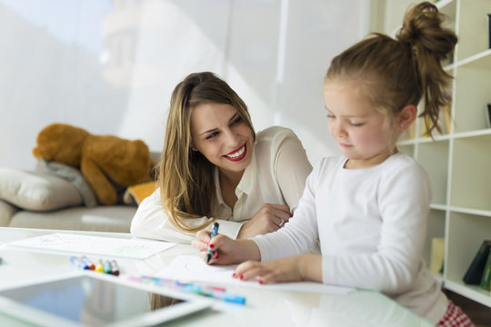 Beautiful mother with her daughter drawing with crayons at home.