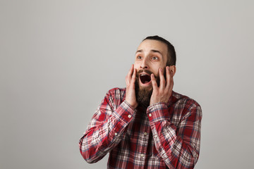 Bearded handsome man frightened in red squared shirt on grey background