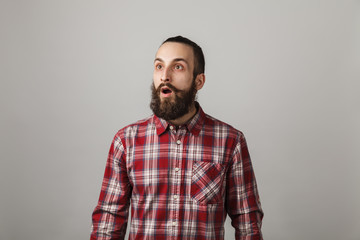 Bearded handsome man scares in red squared shirt on grey background