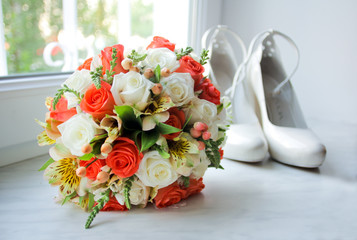 Wedding bouquet with orange and white roses on windowsill. Shoes at the background