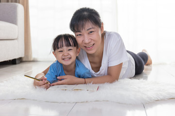 Happy Asian Chinese mother and daughter writing on the floor