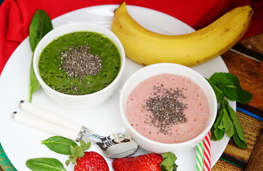smoothies made of banana and spinach and banana and strawberries on wooden background