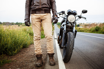 Naklejka premium Young handsome man posing near his motorbike at countryside road.