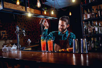 Barman hipster with a beard makes  cocktail in the restaurant bar.