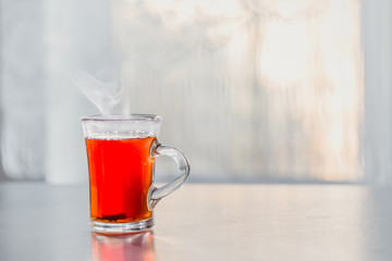 a glass of steaming hot tea on the table against the window.