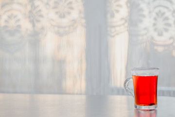 a glass of steaming hot tea on the table against the window.