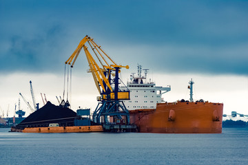 Fototapeta premium Large orange cargo ship loading with a coal in the port