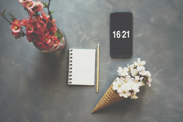 Flowers in ice cream cone with smartphone and notebook on cement background