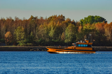 Obraz premium Orange pilot ship sailing past the autumn trees in Europe