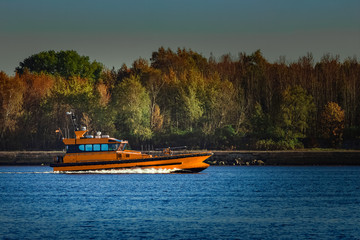 Fototapeta premium Orange pilot ship sailing past the autumn trees in Europe