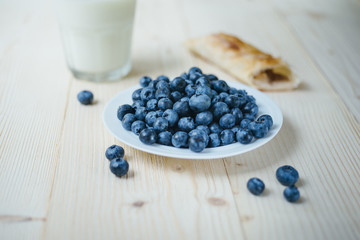 Rustic healthy breakfast with blueberry, small loaf and milk in a glass on a wooden table. Glass of milk with ripe berries. Healthy breakfast with vital vitamins.